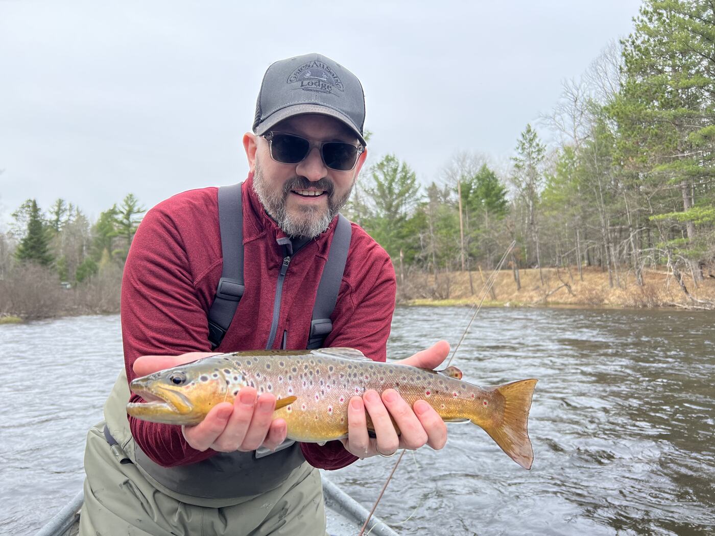 Chris holding a brown trout in a drift boat on the Au Sable