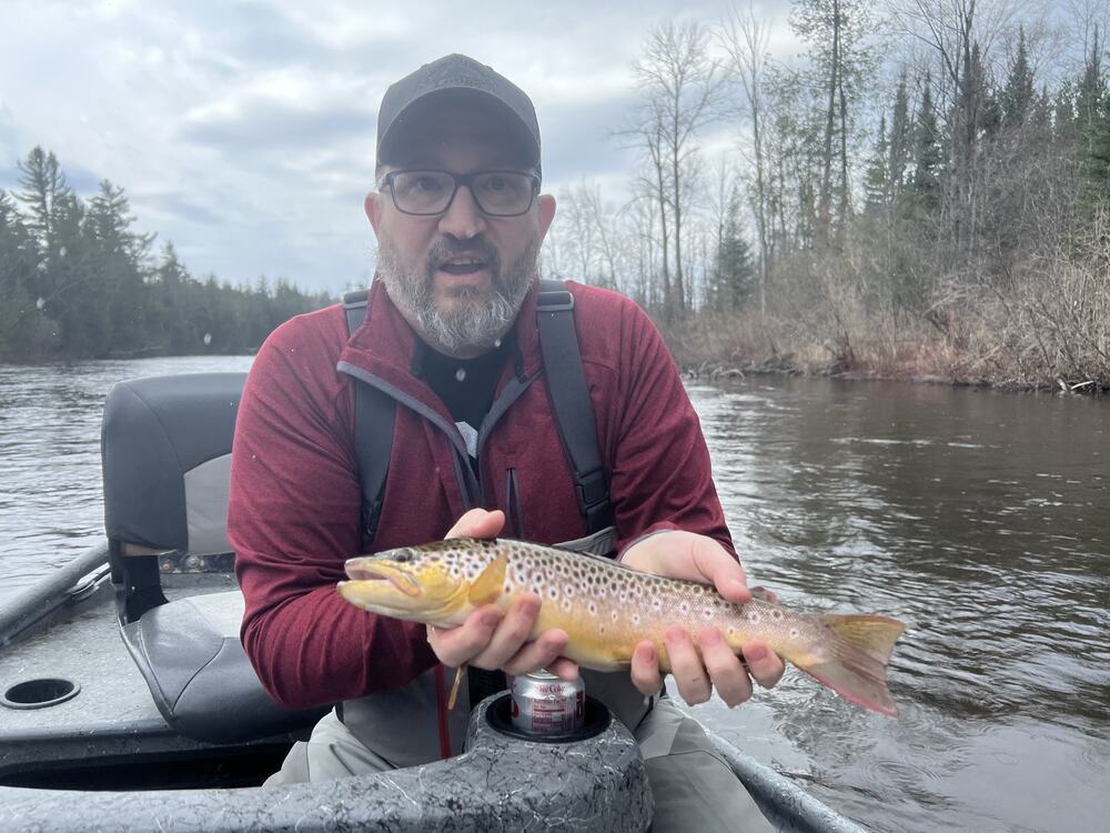 Chris holding a brown trout in a drift boat on a guided Au Sable trip